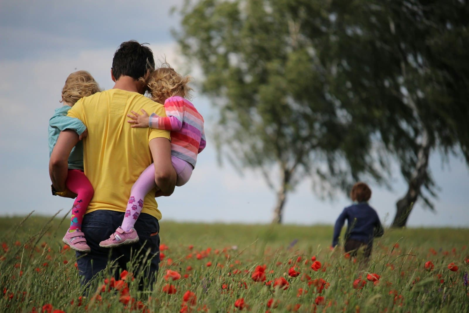 A father carrying two children through a poppy field